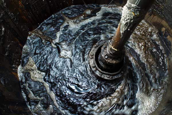 close up of industrial pump stirring dark oil in a tank